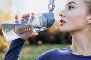 fitness no parque, garota bebe água de uma garrafa, close-up.