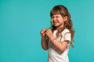 lindo pequeno menina vestindo dentro uma branco camiseta é posando contra uma azul estúdio fundo. foto