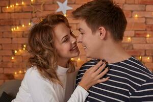 feliz amoroso casal relaxante em cama às lar, jovem mulher tocante sorridente bonito homem face, olhando dentro a olhos. foto