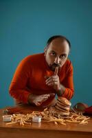 fechar-se retrato do uma meia idade homem com barba, vestido dentro uma vermelho gola alta, posando com hambúrgueres e francês fritas. azul fundo. velozes Comida. foto