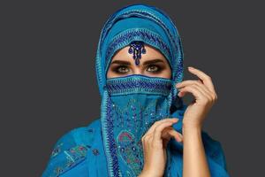 estúdio tiro do uma jovem lindo mulher vestindo a azul hijab decorado com lantejoulas e joia. árabe estilo. foto