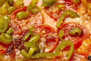 fechar-se do picante pizza com calabresa, Pimenta jalapeno, tomate molho e mozzarella foto
