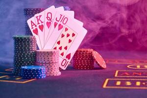 ganhando combinação dentro pôquer inclinado em colori salgadinhos pilhas em azul cobrir do jogando mesa. preto, fumaça fundo, vermelho e azul luzes de fundo. casino. foto