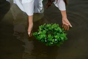 fechar-se do mulher dentro branco vestir dentro a água. arte mulher com guirlanda dentro rio. molhado bruxa menina dentro a lago foto