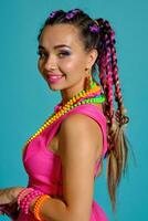 adorável menina com uma multicolorido tranças Penteado e brilhante inventar, posando dentro estúdio contra uma azul fundo. foto