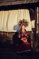 morena menina dentro uma Preto e vermelho bordado ucraniano autêntico nacional traje e uma guirlanda do flores é posando contra uma terraço. fechar-se. foto