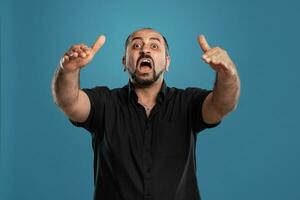 fechar-se retrato do uma moreno meia idade homem com barba, vestido dentro uma Preto camiseta e posando contra uma azul fundo. foto