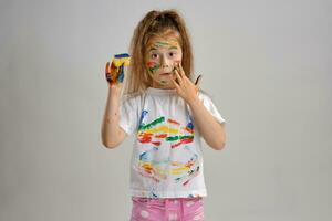 pequeno menina dentro branco pintado camiseta, com colori face é jogando com uma esponja encharcado dentro pintar. isolado em branco. fechar-se. foto