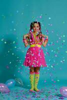 adorável menina com uma multicolorido tranças Penteado e brilhante inventar, posando dentro estúdio com ar balões e confete contra uma azul fundo. foto