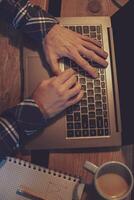jovem homem bebendo café dentro cafeteria e usando computador portátil. do homem mãos foto