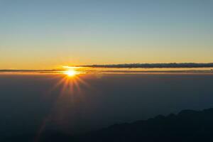 pôr do sol acima horizonte linha com Sol configuração baixa atrás montanhas. foto