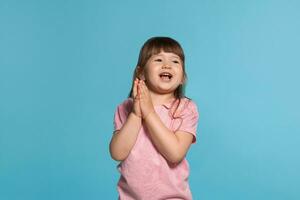 lindo pequeno menina vestindo dentro uma Rosa camiseta é posando contra uma azul estúdio fundo. foto