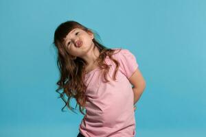 lindo pequeno menina vestindo dentro uma Rosa camiseta é posando contra uma azul estúdio fundo. foto