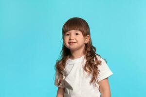 lindo pequeno menina vestindo dentro uma branco camiseta é posando contra uma azul estúdio fundo. foto