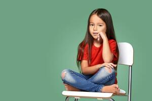 pequeno menina vestindo vermelho t-curto e posando em cadeira foto