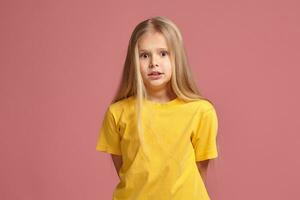 pequeno menina dentro uma amarelo camiseta. parece intrigado foto