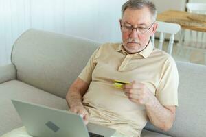 Senior homem compras conectados usando computador portátil pagando com crédito cartão. velho avô comprando em Internet entrar crédito cartão detalhes. conectados compras Entrega serviço. Mais velho geração moderno tecnologia uso. foto