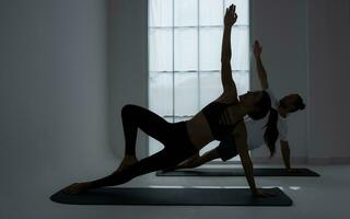 silhueta do uma jovem casal praticando ioga dentro a sala. foto