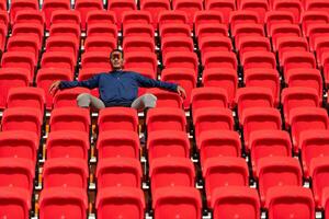 Desativado atletas dentro uma azul camisa sentado em a vermelho assentos às a estádio, preparar para corrida treinamento. foto