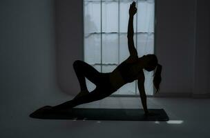 silhueta do uma jovem mulher praticando ioga dentro a sala. foto