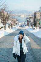 mulher turista visitando dentro hakodate, viajante dentro suéter passeios turísticos hachiman zaka declive com neve dentro inverno. ponto de referência e popular para atrações dentro Hokkaido, Japão. viagem e período de férias conceito foto