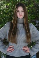 Adolescência menina braços akimbo e olhando às Câmera. adolescente vestindo dentro suéter em pé dentro pinho floresta foto
