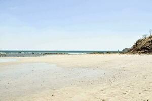 uma arenoso de praia com uma penhasco em a horizonte foto