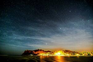 a noite céu sobre a de praia e a luzes do a Cidade foto