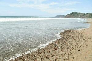 uma arenoso de praia com ondas e pedras foto