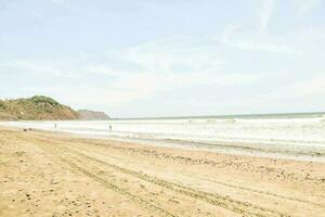 uma arenoso de praia com ondas e pedras foto