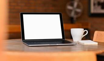 laptop de tela em branco de maquete com café e notebook em cima da mesa, retirado da frente. foto