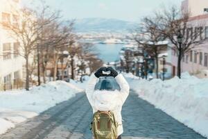 mulher turista visitando dentro hakodate, viajante dentro suéter passeios turísticos hachiman zaka declive com neve dentro inverno. ponto de referência e popular para atrações dentro Hokkaido, Japão. viagem e período de férias conceito foto