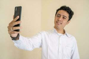 indonésio homem vestem branco roupas com selfie olhando para Câmera foto