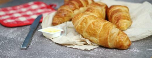 uma pilha de deliciosos croissants frescos servidos com manteiga em uma mesa cinza. foto