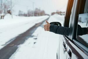 feliz viajante dirigindo carro em Nevado estrada e gesto dedo acima, mulher turista desfrutando neve floresta Visão a partir de a carro janela dentro inverno temporada. inverno viagem, estrada viagem, explorando e período de férias conceitos foto