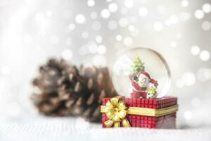 Natal bolas, santa claus dentro uma neve globo, e pinho cones em uma branco pano, conjunto contra uma vermelho fundo e requintado bokeh. Novo ano celebração atmosfera, sobre do importante dia. foto