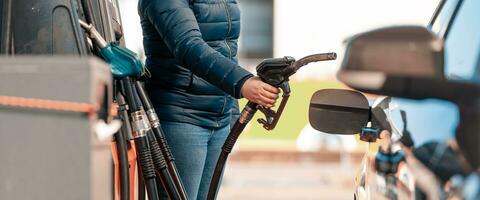 Alto preços do gasolina e diesel combustível ath a gasolina estação, jovem mulher reabastecimento a carro, econômico crise conceito foto