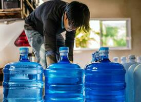 bebendo água Claro e limpar \ limpo dentro azul galão arranjado dentro uma linha preparar para lift para dentro a costas do uma transporte caminhão purificado bebendo água dentro a Produção linha pequeno o negócio foto