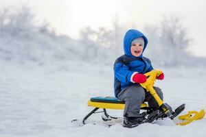 uma pequeno criança é sentado em uma neve lambreta dentro inverno foto