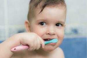 adorável bebê escovar dele dentes com uma escova de dente dentro a banheiro foto