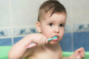 adorável bebê escovar dele dentes com uma escova de dente dentro a banheiro foto