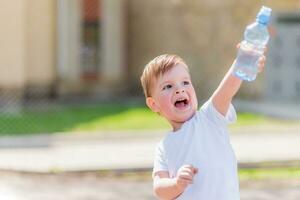 alegre criança bebidas Claro água a partir de uma garrafa em uma ensolarado dia dentro natureza foto
