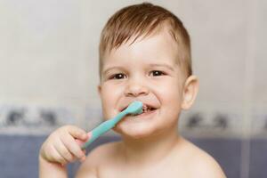adorável bebê escovar dele dentes com uma escova de dente dentro a banheiro foto