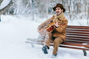 alegre cara jogando guitarra dentro parque dentro inverno foto