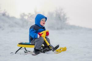 uma pequeno criança é sentado em uma neve lambreta dentro inverno foto