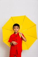 pequeno Garoto moda uma sorridente criança segurando uma amarelo guarda-chuva dentro uma vermelho chinês vestir. chinês Novo ano, chinês Novo ano foto