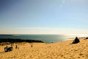 pessoas sentado em a areia dunas perto a oceano foto