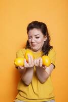 dentro a estúdio, fêmea Individual com uma pateta face segurando amarelo citrino frutas. jovem mulher exibindo uma grupo do fresco cru natural limões para uma Vitamina rico lanche. foto