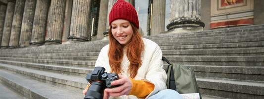 jovem estudante, fotógrafo senta em rua escadas e Verificações dela tiros em profissional Câmera, levando fotos ao ar livre