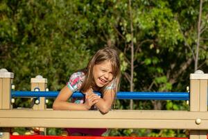 feliz caucasiano pequeno menina do 6 7 anos sorridente e piscando olhando às Câmera em jogar terra sobre verde árvores foto